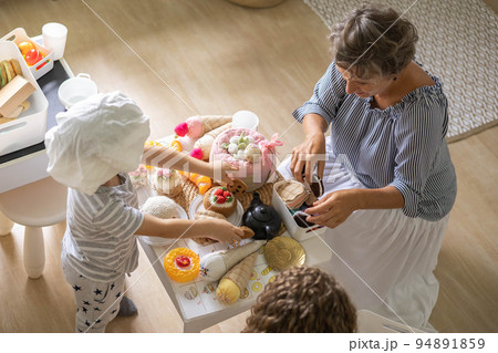 Mother and cute baby boy and girl cooking food at childish kitchen playing chef educational playthings Mother and cute baby boy and girl cooking food at childish kitchen playing chef educational playthings 94891859