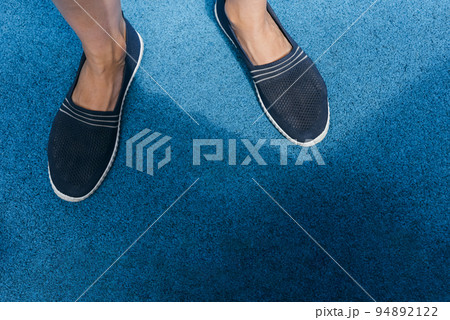 Slip-ons of dark blue color on female legs. Bright blue rubber running track. Slip-ons of dark blue color on female legs. Bright blue rubber running track. 94892122