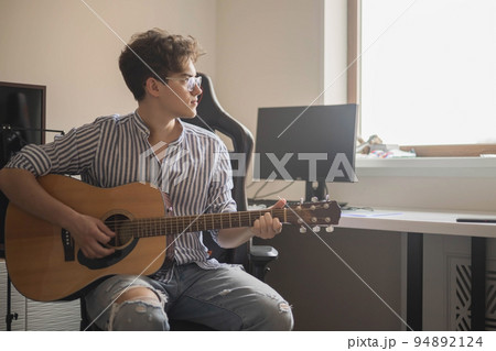 Male teenager singing song playing acoustic guitar reading text on smartphone application screen Male teenager singing song playing acoustic guitar reading text on smartphone application screen 94892124