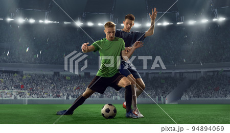 Fight for the ball. Two male soccer, football players dribbling ball at the stadium during sport match at crowded stadium. Sport competition, energy. Fight for the ball. Two male soccer, football players dribbling ball at the stadium during sport match at crowded stadium. Sport competition, energy. 94894069