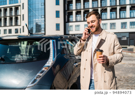Handsome man with cup of coffee in his hand talking on the phone while standing near his car 94894073