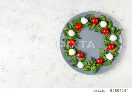 Caprese salad in the form of a Christmas wreath. Festive tomato mozzarella and basil appetizer on grey plate. 94897144