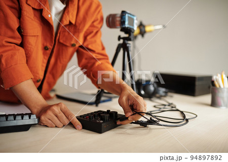 Unrecognizable male influencer standing at desk in studio connecting microphone with mixing console 94897892
