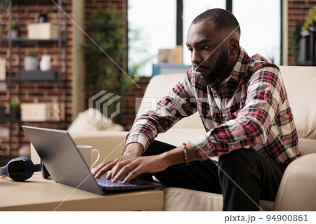 African american man browsing internet on laptop, working on social media app to create business report on online browser. Doing remote freelance on computer and analyzing management presentation. 94900861