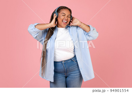 Happy Black Plus Size Woman Singing Wearing Headphones, Pink Background Happy Black Plus Size Woman Singing Wearing Headphones, Pink Background 94901554