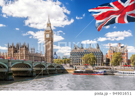 Big Ben with bridge over Thames and flag of England against blue sky in London, England, UK 94901651