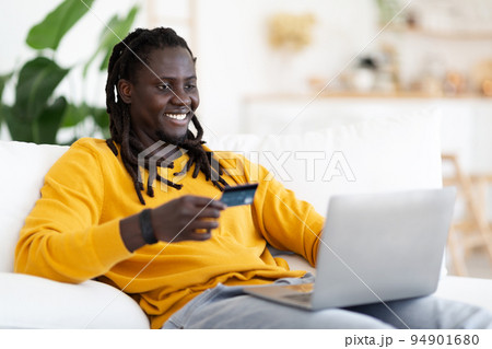 Black Man Making Online Payments With Laptop And Credit Card At Home Black Man Making Online Payments With Laptop And Credit Card At Home 94901680