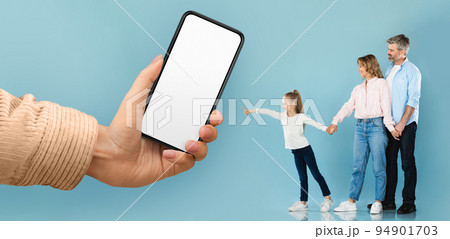 Cheerful young european man and woman with little girl pointing at huge smartphone with blank screen in hand Cheerful young european man and woman with little girl pointing at huge smartphone with blank screen in hand 94901703