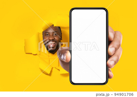Recommendation. Excited black man holding big smartphone with blank screen through torn yellow paper hole 94901706