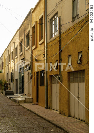 driveway, sidewalk and cobblestone in a small neighborhood, adjoining yellow and mustard-colored houses, at sunset 94902363
