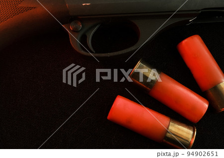 Trigger of a rifle on black background with red lightning with Shotgun shells on a black surface. Ammunition for 12 gauge smoothbore weapons. Hunting ammunition. Dark background. Trigger of a rifle on black background with red lightning with Shotgun shells on a black surface. Ammunition for 12 gauge smoothbore weapons. Hunting ammunition. Dark background. 94902651