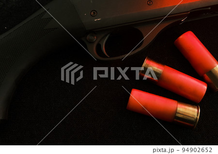 Trigger of a rifle on black background with red lightning with Shotgun shells on a black surface. Ammunition for 12 gauge smoothbore weapons. Hunting ammunition. Dark background. Trigger of a rifle on black background with red lightning with Shotgun shells on a black surface. Ammunition for 12 gauge smoothbore weapons. Hunting ammunition. Dark background. 94902652