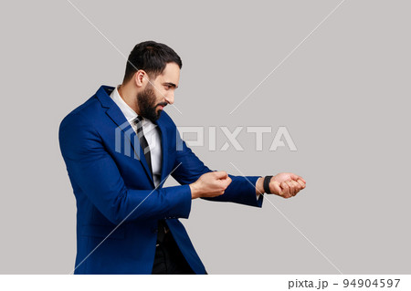 Side view of bearded man looking diligent and strong, standing in attack or pulling hands gesture and looking forward, wearing official style suit. Indoor studio shot isolated on gray background. Side view of bearded man looking diligent and strong, standing in attack or pulling hands gesture and looking forward, wearing official style suit. Indoor studio shot isolated on gray background. 94904597