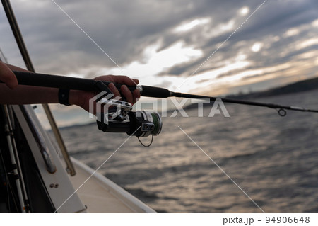 Fishing rod wheel closeup, man fishing with a beautiful sunrise behind him 94906648