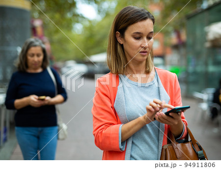 Focused young business woman using smartphone while walking outoors Focused young business woman using smartphone while walking outoors 94911806