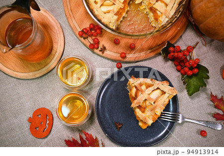 Top view. A piece of homemade classic American sweet pumpkin pie with apples and crispy crust lattice, for Thanksgiving Day and two cups of lemon tea, on a served table with linen tablecloth. Tea time 94913914