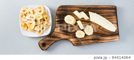 Banana slices on a cutting board and banana chips on a saucer on the table. Fast food. Web banner 94914064