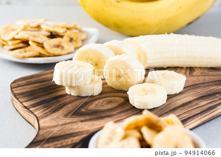 Banana slices on a cutting board for making banana chips on the table. Fast food. Banana slices on a cutting board for making banana chips on the table. Fast food. 94914066
