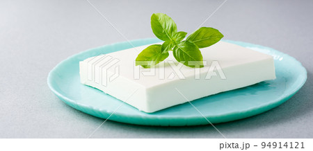 A piece of fresh feta cheese and basil leaves on a plate on the table. Ingredient for Greek salad. Web banner A piece of fresh feta cheese and basil leaves on a plate on the table. Ingredient for Greek salad. Web banner 94914121