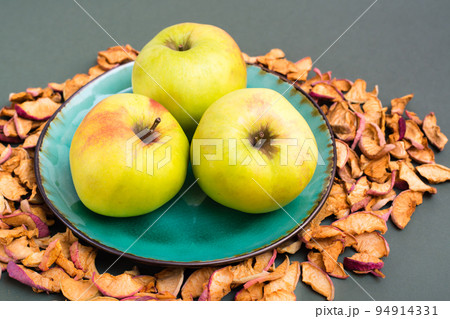 Fresh apples on a plate and pieces of dry apples around on a green background 94914331