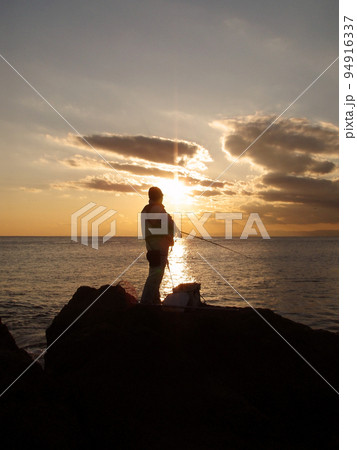 相模湾に落ちる夕陽、夕まずめ時を狙い続ける磯にたつクロダイ釣り人のシルエット。 94916337