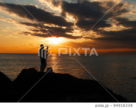 相模湾に落ちる夕陽、夕まずめ時を狙い続ける磯にたつクロダイ釣り人のシルエット。 94916338