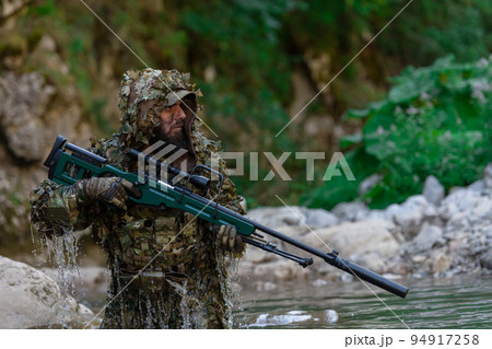 A military man or airsoft player in a camouflage suit sneaking the river and aims from a sniper rifle to the side or to target. A military man or airsoft player in a camouflage suit sneaking the river and aims from a sniper rifle to the side or to target. 94917258