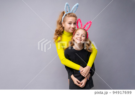 Close-up portrait two cheerful pretty young girls with bunny ears in yellow Close-up portrait two cheerful pretty young girls with bunny ears in yellow 94917699