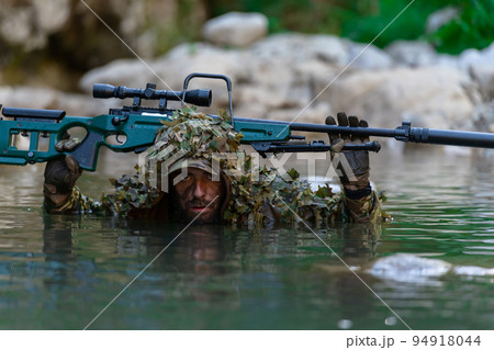 A military man or airsoft player in a camouflage suit sneaking the river and aims from a sniper rifle to the side or to target. A military man or airsoft player in a camouflage suit sneaking the river and aims from a sniper rifle to the side or to target. 94918044
