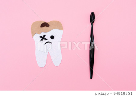 A plastic toothbrush and a felt-cut out sad tooth with decay. Flat lay. Pink background. Copy space. Concept of hygiene of the oral cavity 94919551