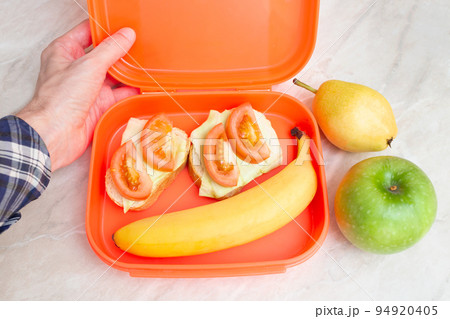 The man in the shirt opened a lunch box with fruit and vegetables. Healthy snack. Proper nutrition. Top view. Lunch at work. The man in the shirt opened a lunch box with fruit and vegetables. Healthy snack. Proper nutrition. Top view. Lunch at work. 94920405