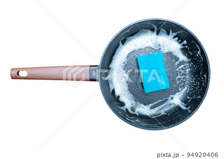 Washing a black frying pan with a wooden handle. Sponge for washing dishes and lots of foam. Isolated on a white background. Top view. Washing a black frying pan with a wooden handle. Sponge for washing dishes and lots of foam. Isolated on a white background. Top view. 94920406