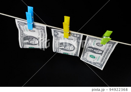 One and two dollar banknotes fastened with clothespins are dried on clotheslines on a dark background 94922368