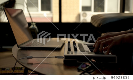 Woman hands playing on small midi controller, producer of music with laptop on table. Closeup of 94923855