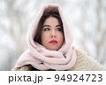 Portrait of thoughtful brunette young woman dressed in white fur coat and light pink scarf on head looking away. Romantic adult female model on winter day outdoors. Selective soft focus on foreground 94924723