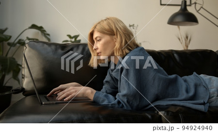 Young woman using laptop, chilling on a sofa in living room. Woman in jeans clothes concentrated Young woman using laptop, chilling on a sofa in living room. Woman in jeans clothes concentrated 94924940