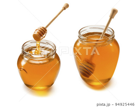 Two glass jars with liquid honey set isolated on white background. Wooden dippers Two glass jars with liquid honey set isolated on white background. Wooden dippers 94925446