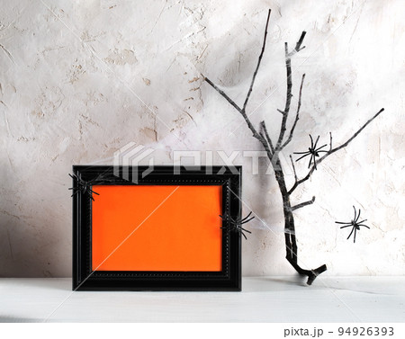 Hallowen minimal image. Black frame with orange empty space for text, spiders, dry twig in cobwebs on white wooden table on neutral backdrop. Holiday card or party invitation. Mock up. Horizontal shot Hallowen minimal image. Black frame with orange empty space for text, spiders, dry twig in cobwebs on white wooden table on neutral backdrop. Holiday card or party invitation. Mock up. Horizontal shot 94926393