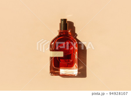 Transparent perfume bottle with red filling on a pastel beige background in the sunlight. Flat lay, top view. Luxury presentation mockup. Beautiful opened glass of aroma water 94928107