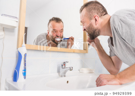 Man brushing his teeth in bathroom Man brushing his teeth in bathroom 94929399