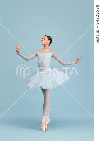 Portrait of tender young ballerina dancing, performing isolated over blue studio background. Standing on pointe 94929588