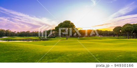Golf course panorama at sunset with beautiful sky. Scenic panoramic view. Golf course with pine trees 94930166