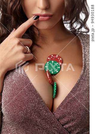 Brunette woman wearing in shiny brown dress. There are some green and red chips on her breast. Isolated on white background. Casino, poker. Close-up. 94930188