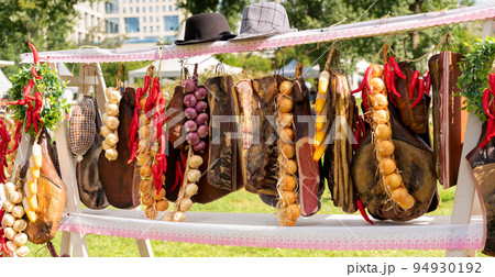 Market display with large pieces of meat, bacon, jamon and other delicacies and condiments hung Market display with large pieces of meat, bacon, jamon and other delicacies and condiments hung 94930192