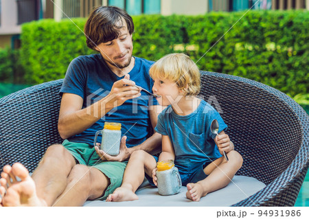 Father and son eat dessert with chia seeds and mangoes by the pool in the morning. healthy eating, vegetarian food, diet and people concept Father and son eat dessert with chia seeds and mangoes by the pool in the morning. healthy eating, vegetarian food, diet and people concept 94931986