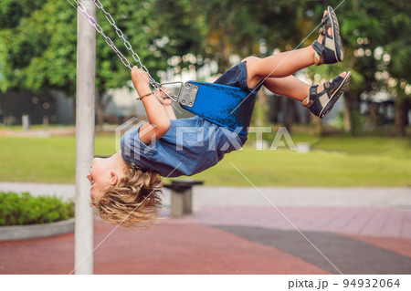 Funny kid boy having fun with chain swing on outdoor playground. child swinging on warm day. Active leisure with kids. Boy wearing casual colorful school kid clothes Funny kid boy having fun with chain swing on outdoor playground. child swinging on warm day. Active leisure with kids. Boy wearing casual colorful school kid clothes 94932064
