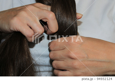 A girl with long dark hair is braiding her hair. Close-up hands. Hair care. Hair loss problem. 94932124