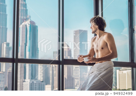 Man wakes up in the morning in an apartment in the downtown area with a view of the skyscrapers and drinks coffee. Life in the noise of the big city concept. Not enough sleep 94932499