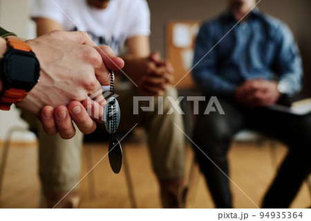 Hands with clasped fingers of young depressed man with two medallions on chain 94935364