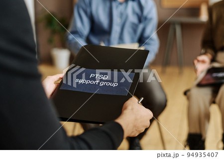 Selective focus on black folder with sticker saying PTSD support group 94935407